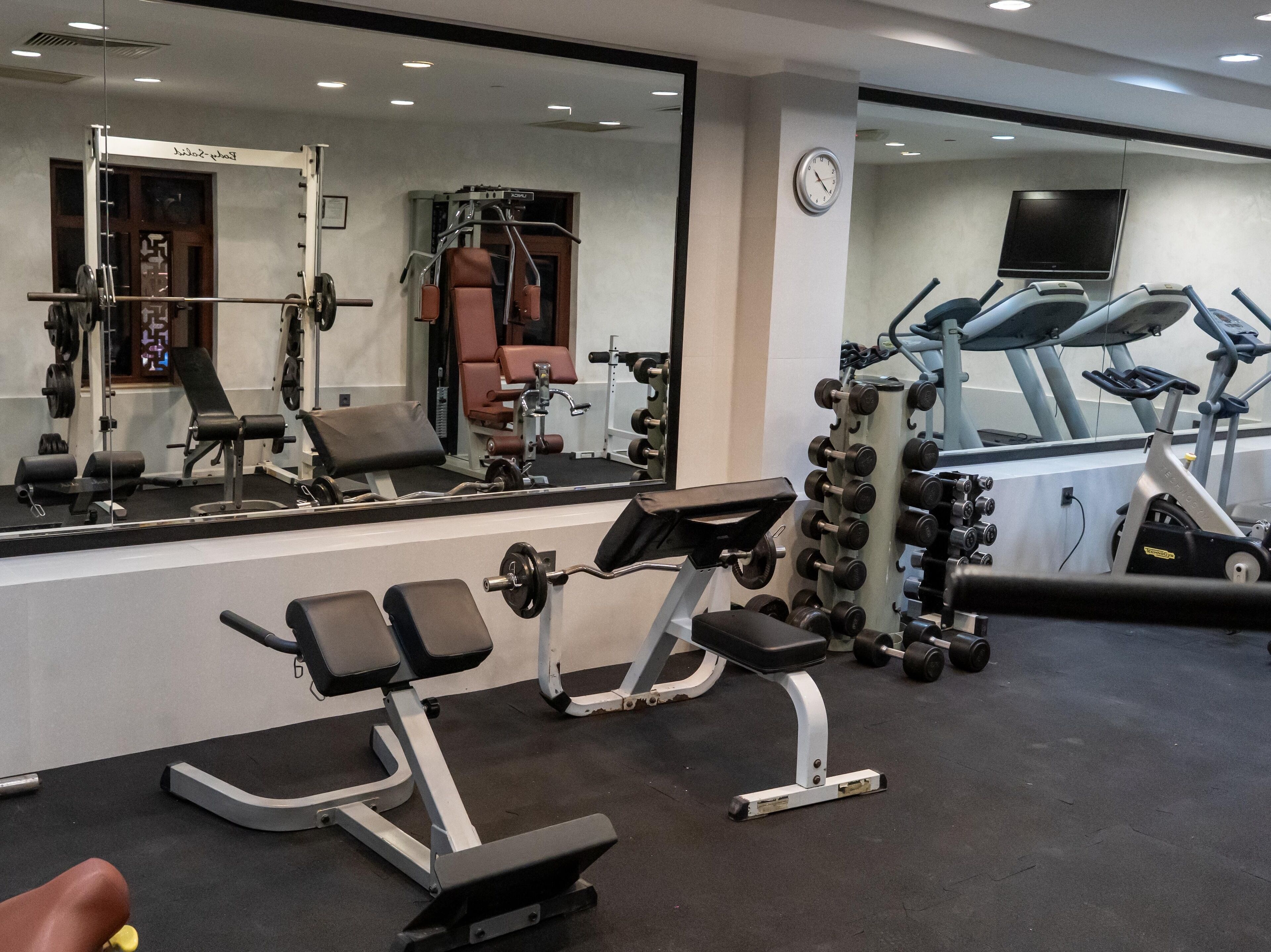 A gym with exercise equipment, a mirror, and a clock on the wall.