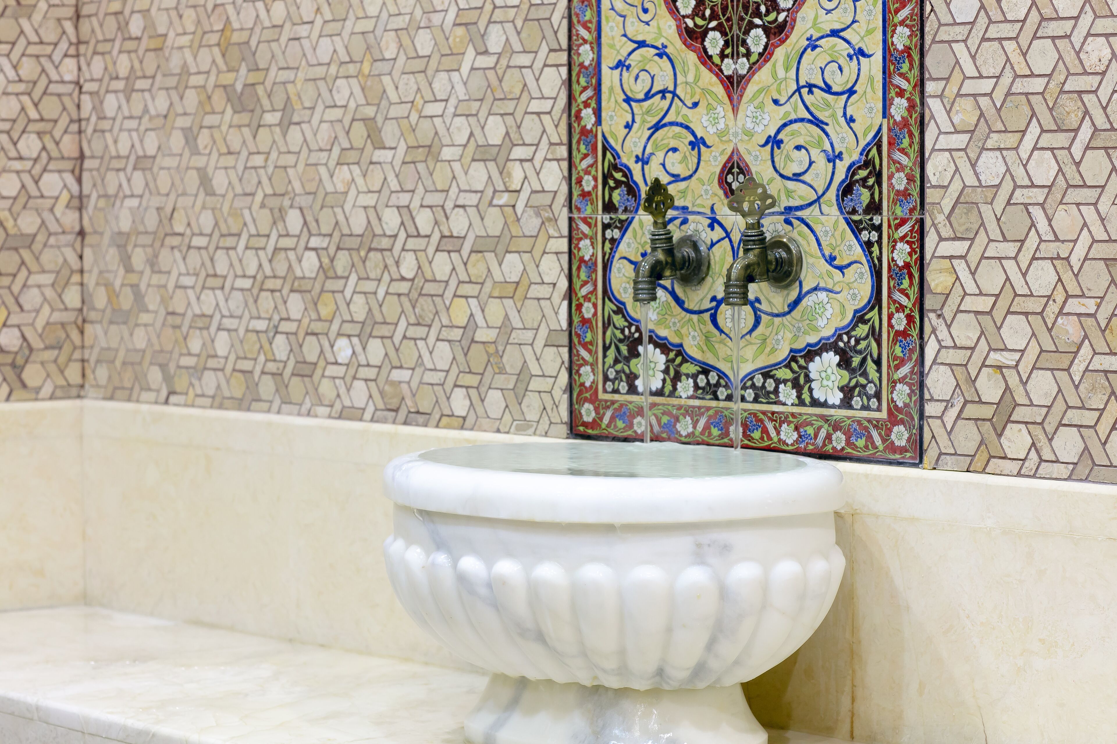A bathroom with a white pedestal sink and a decorative tile wall.