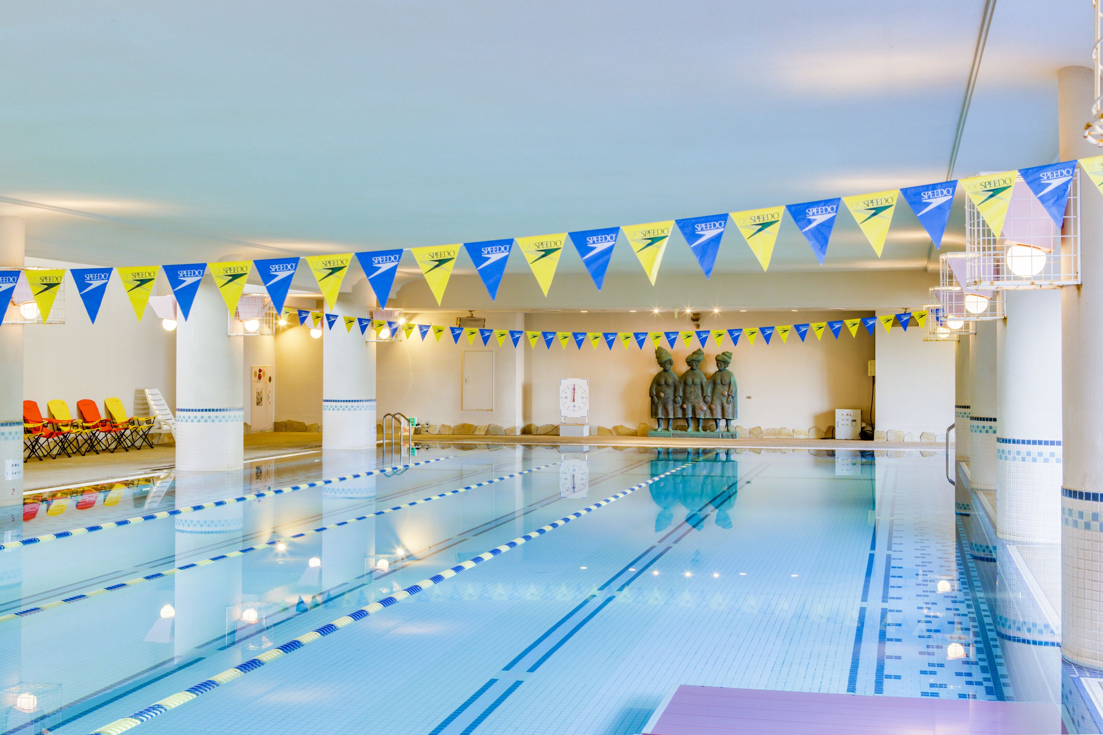 Une piscine intérieure dotée de couloirs délimités, d’un espace détente avec des chaises et de drapeaux décoratifs.