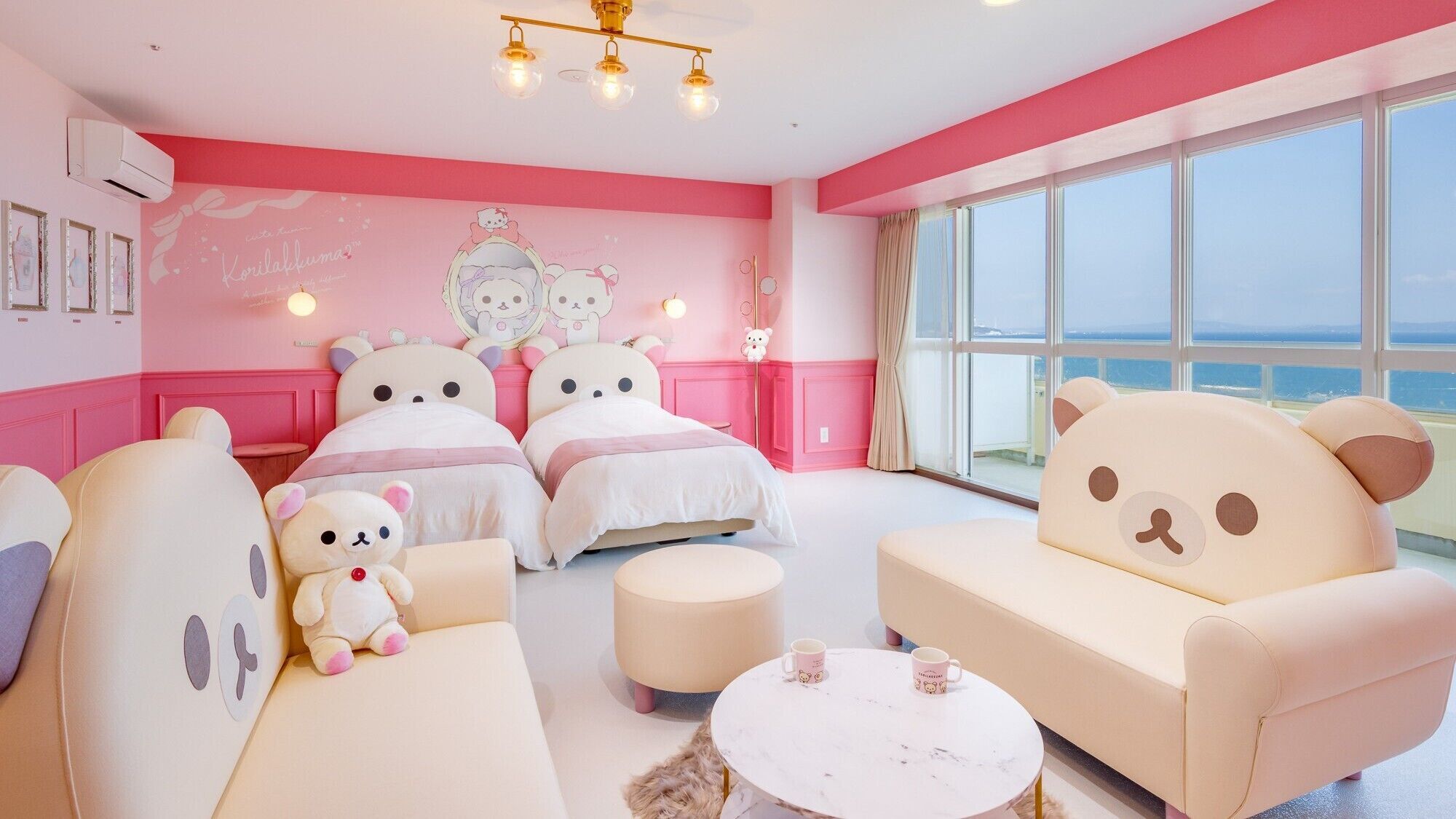 Een hotelkamer in roze tinten, met een groot raam, een bank, een bed en een teddybeer.