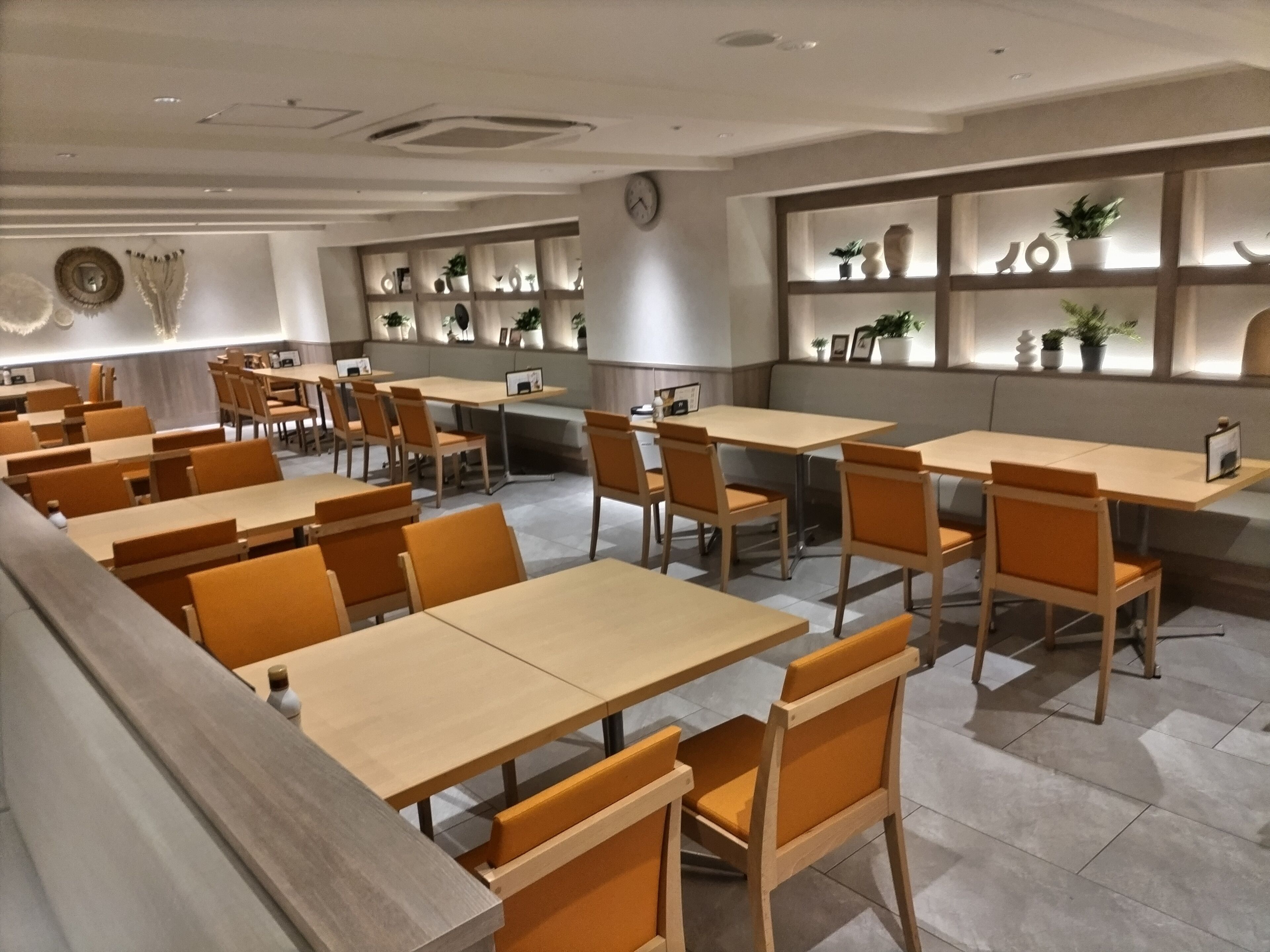 A modern restaurant interior with wooden tables and chairs, a counter area, and shelves with decorative items.