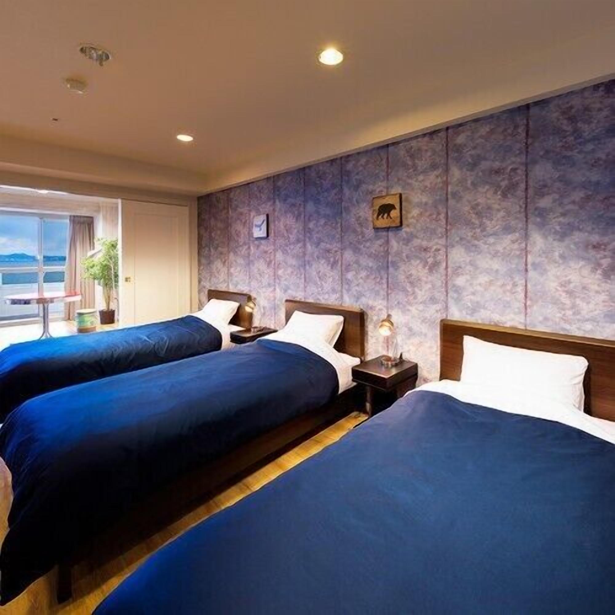 Een hotelkamer met twee bedden, een nachtkastje met lamp, een kleintje tafeltje met een plant en een raam met uitzicht.