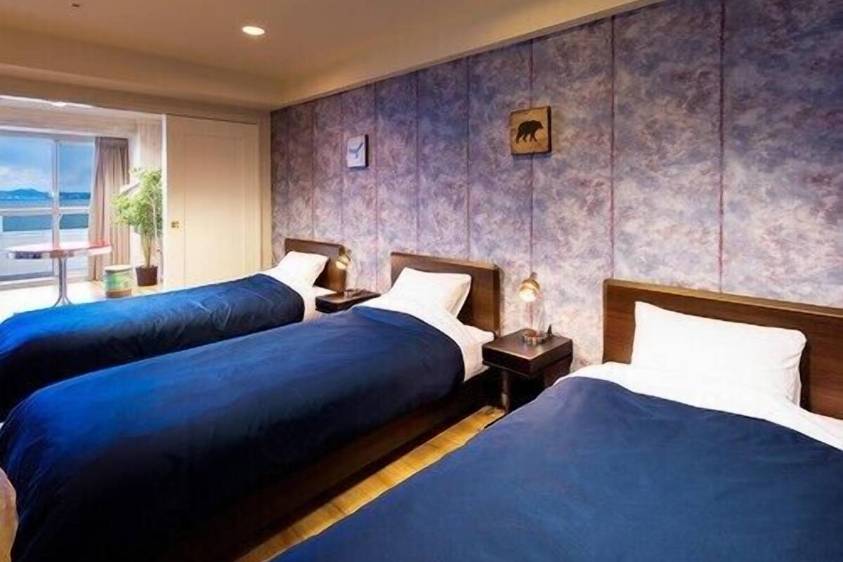 Een hotelkamer met twee bedden, een nachtkastje met lamp, een kleintje tafeltje met een plant en een raam met uitzicht.