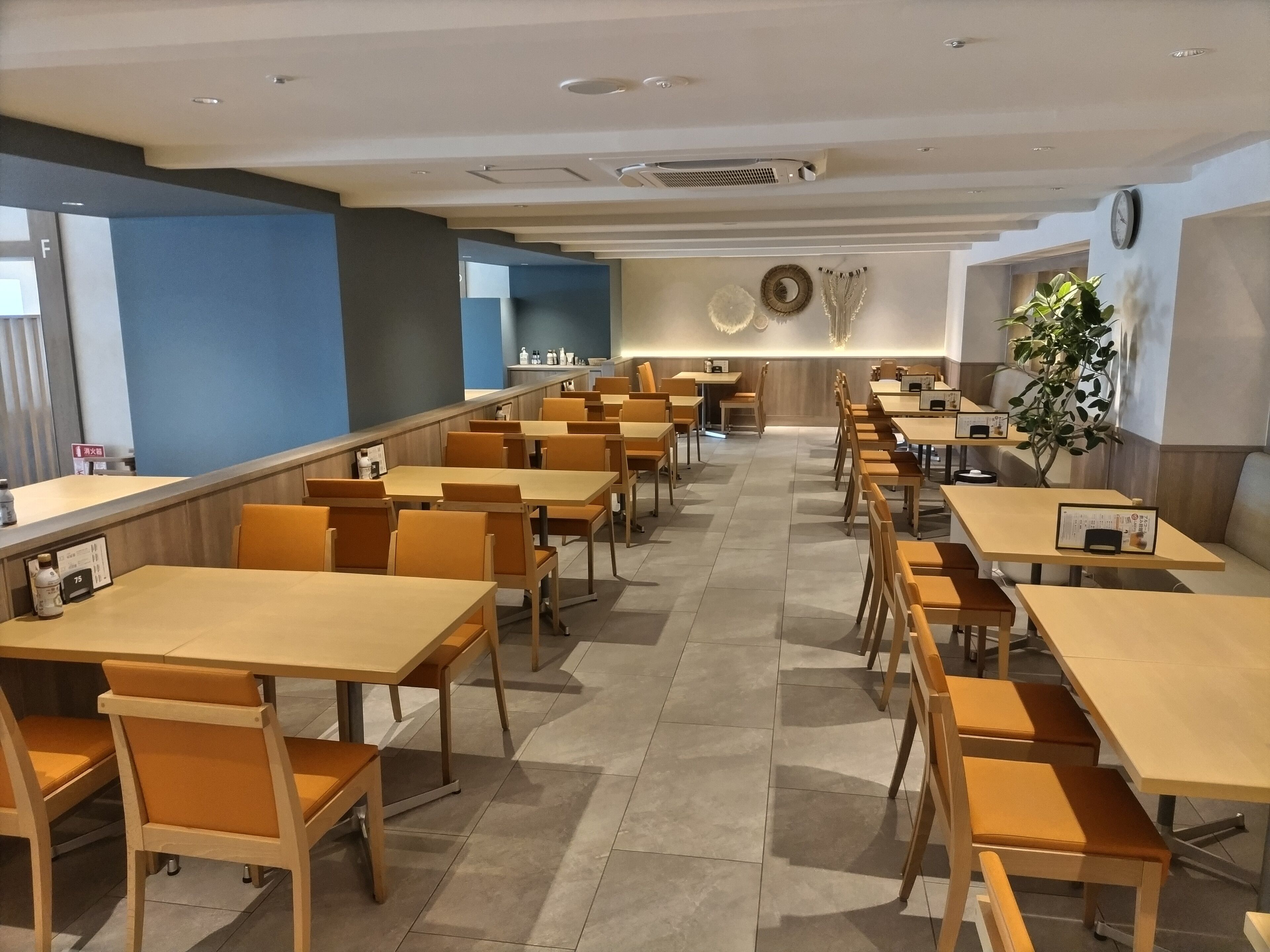 Un restaurante moderno con varias mesas y sillas de madera, una pared de acento azul y un reloj en la pared.