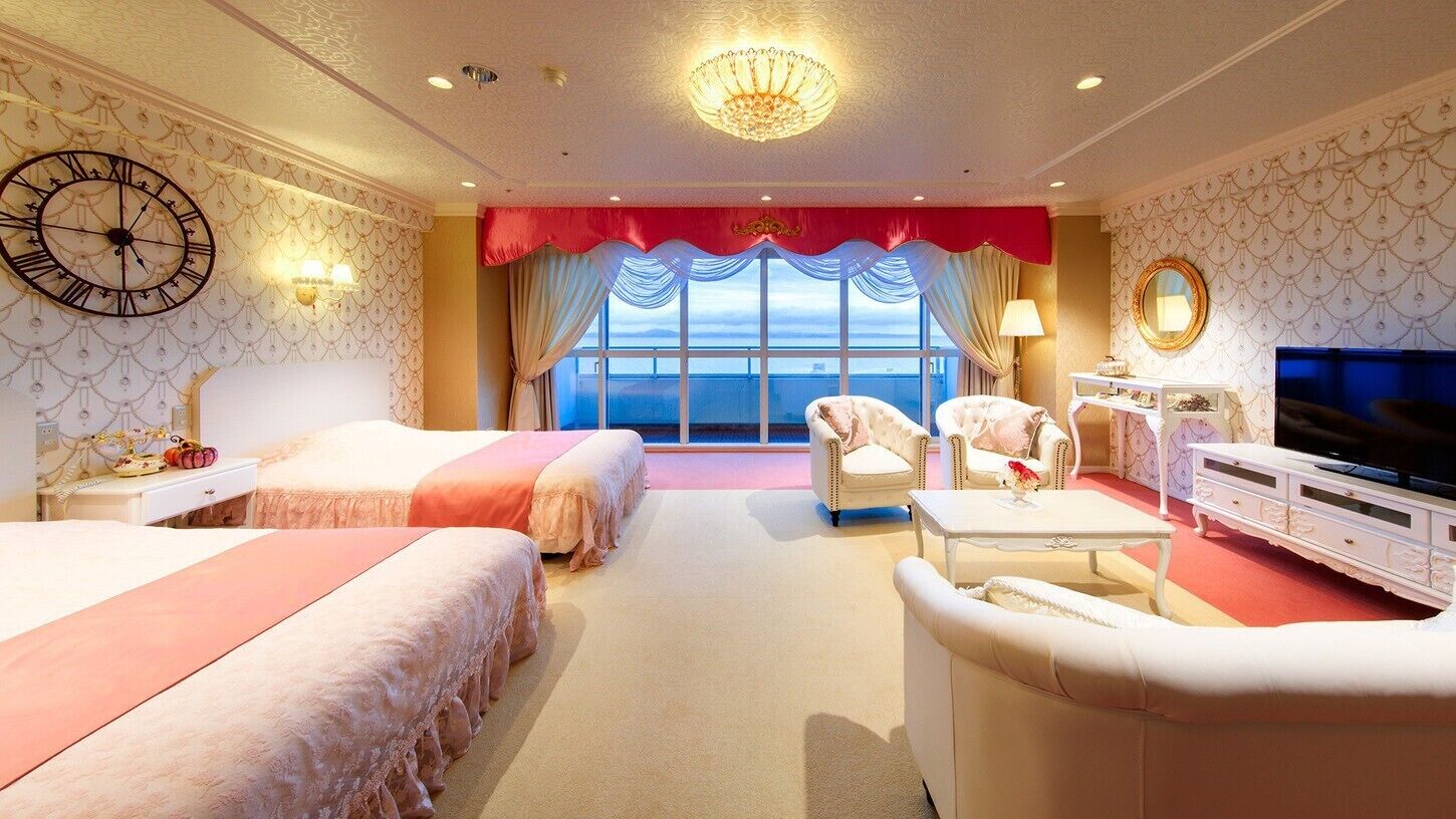 Een hotelkamer met twee bedden, een televisie, een kroonluchter en uitzicht op zee.