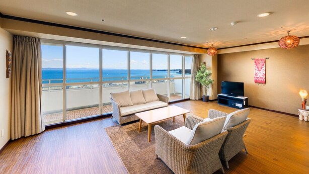 Een ruime woonkamer met een groot raam met uitzicht op zee, een bank, twee fauteuils, een salontafel en een flatscreen televisie.