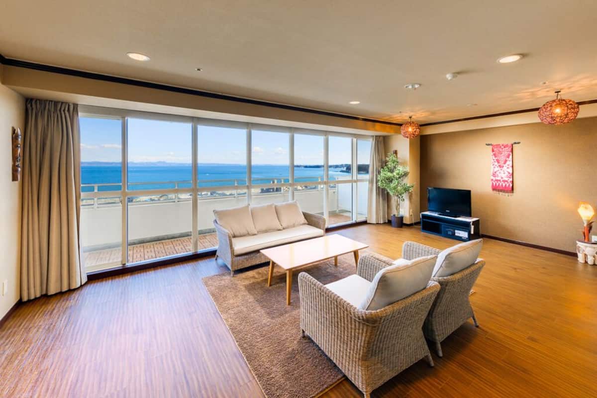 Een ruime woonkamer met een groot raam met uitzicht op zee, een bank, twee fauteuils, een salontafel en een flatscreen televisie.