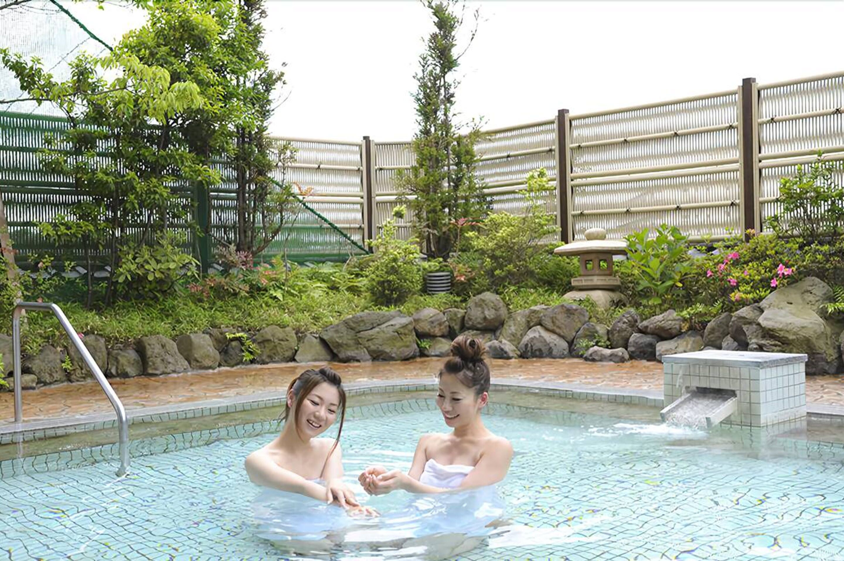 A swimming pool area with a bamboo fence, rocks, and greenery.