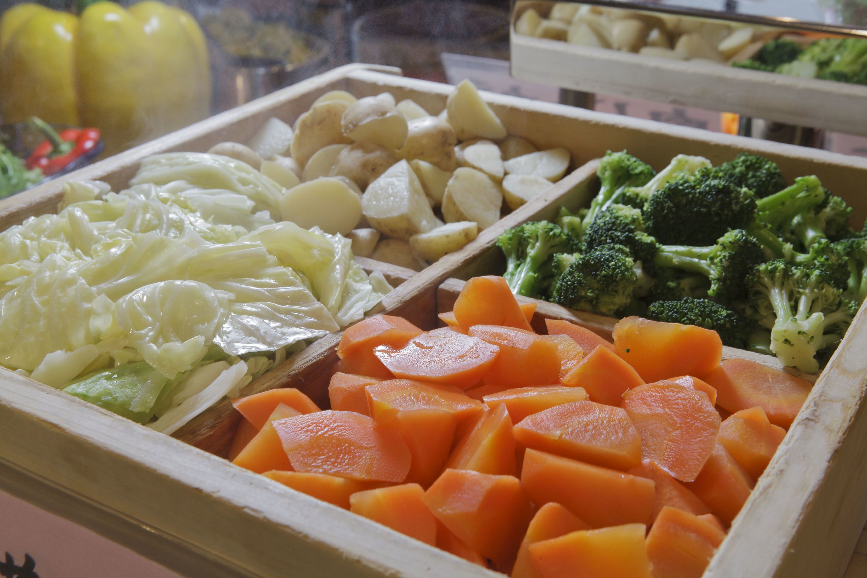 A variety of fresh vegetables including cabbage, carrots, potatoes, and broccoli in a wooden box.