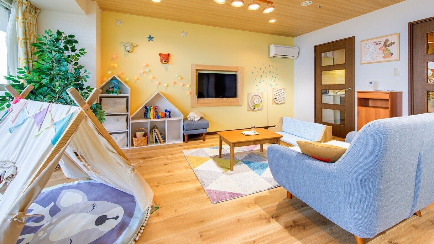 Een gezellige woonkamer met een blauwe bank, een houten salontafel, een klein speelhuisje en een tentachtige constructie.