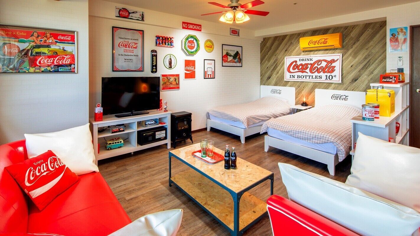 Een kamer met een televisie, twee bedden, een bank en diverse Coca-Cola souvenirs.