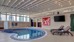 Una piscina interior con sillones de descanso y un televisor grande en la pared.