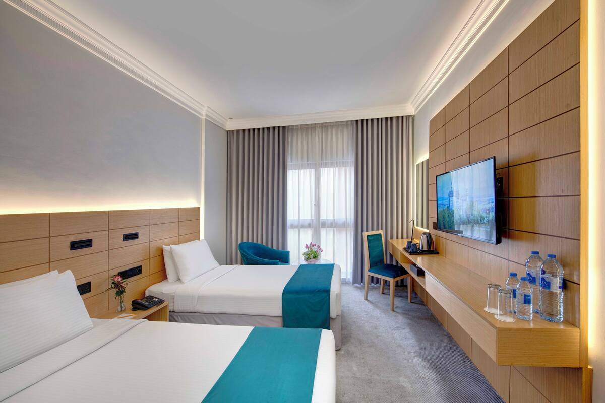 A hotel room with two beds, a desk, a chair, a TV, and a minibar.