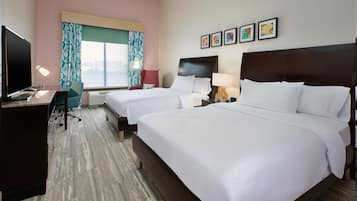 Habitació d'hotel amb dos llits, una taula de treball amb televisió, una cadira i una finestra amb cortines.