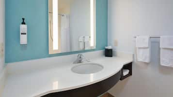 A bathroom with a white sink, a large mirror, a towel rack, and a bottle of shampoo.