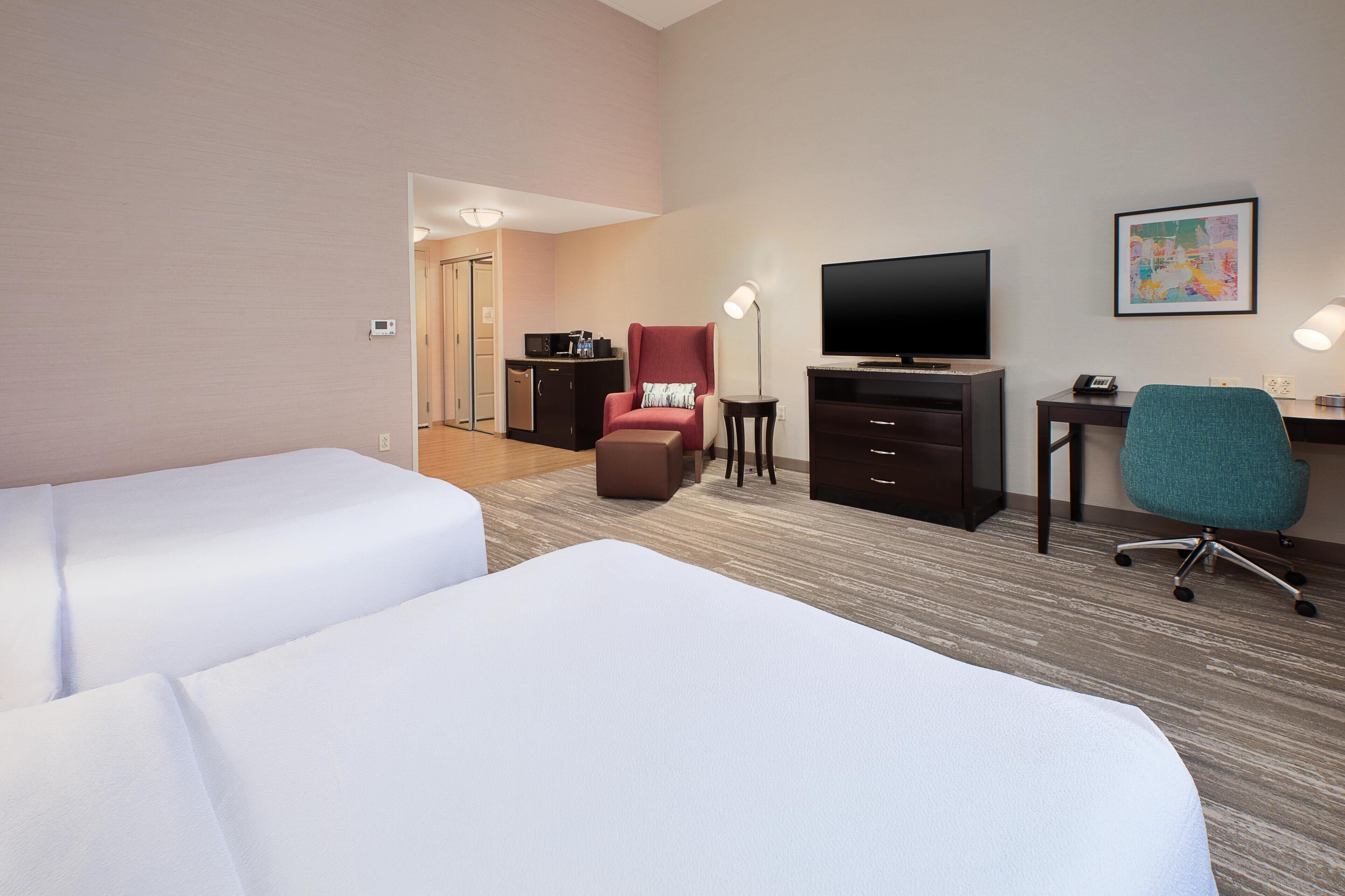 A hotel room with two beds, a TV, a desk with a chair, and a door leading to a hallway.