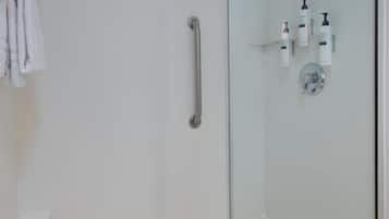 A glass-enclosed shower with a handrail, a toilet, and toiletries on the wall.