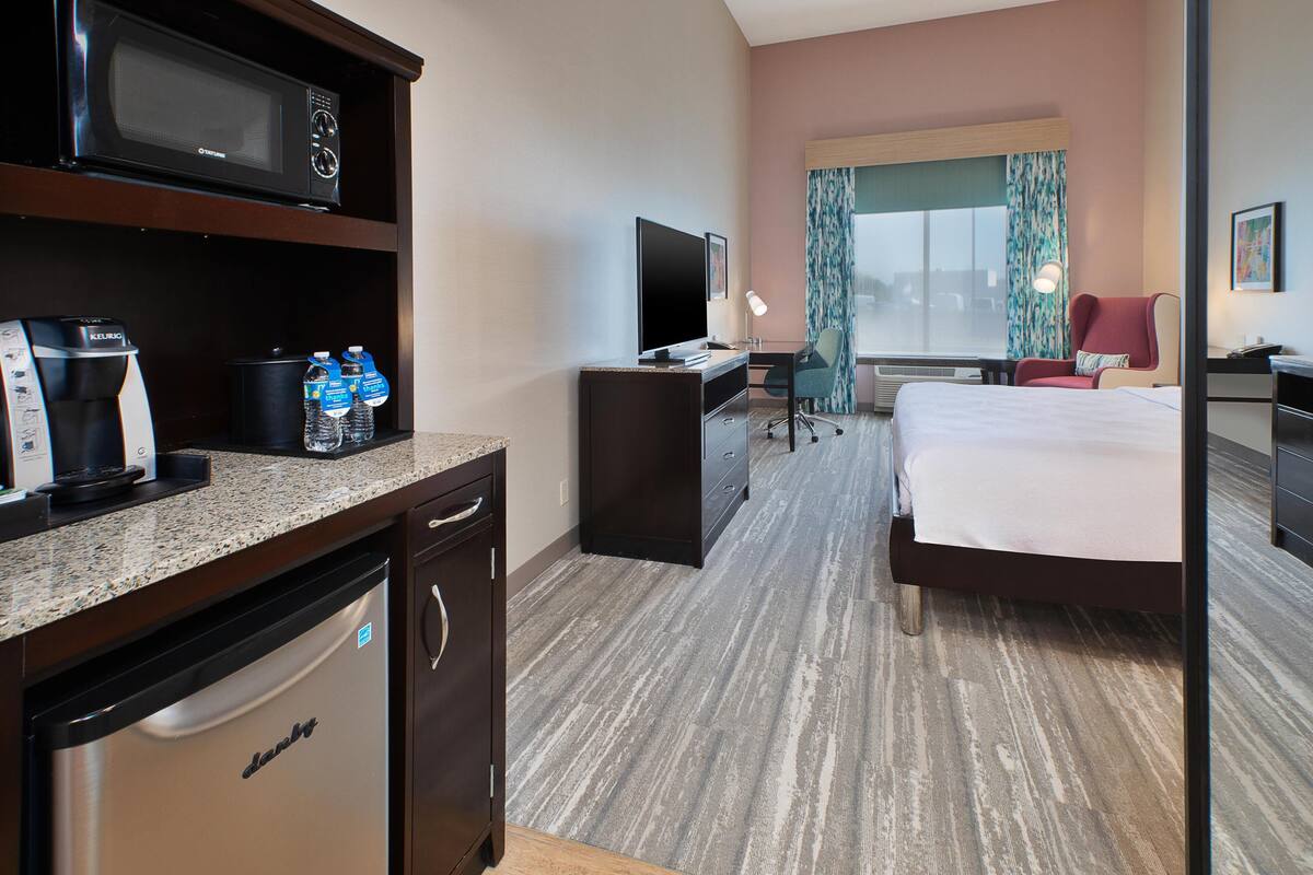 A hotel room with a bed, desk, microwave, coffee maker, and a television.