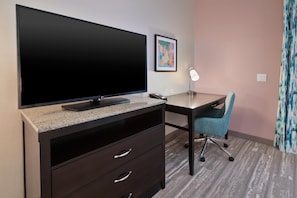 Hotelkamer met een grote flatscreen televisie op een granieten aanrecht, een bureau met stoel, een ingelijst schilderij aan de muur en een lamp.