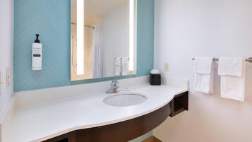 A bathroom with a white sink, a large mirror, a towel rack, and a bottle of shampoo.