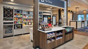 A hotel shop with shelves stocked with snacks, a refrigerated display, and a coffee machine.