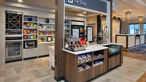A hotel shop with shelves stocked with snacks, a refrigerated display, and a coffee machine. - Hilton Garden Inn Akron (Akron)