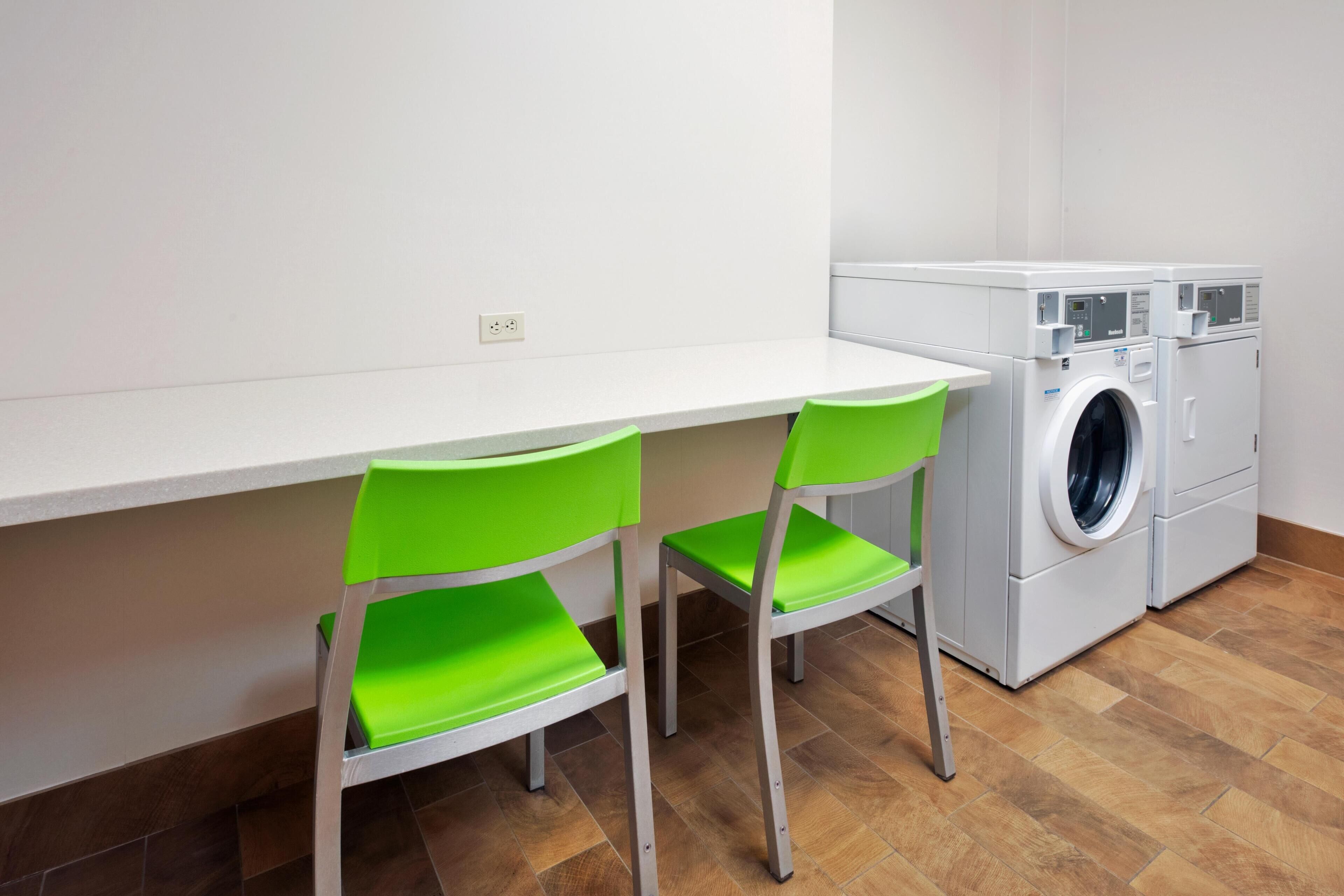 A small laundry area with a washing machine and two green chairs.