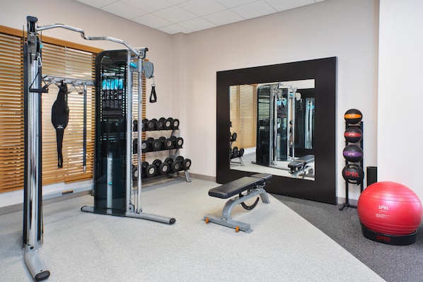 Een sportschool met trainingsapparatuur, een bank, een rode trainingsbal en een spiegel.