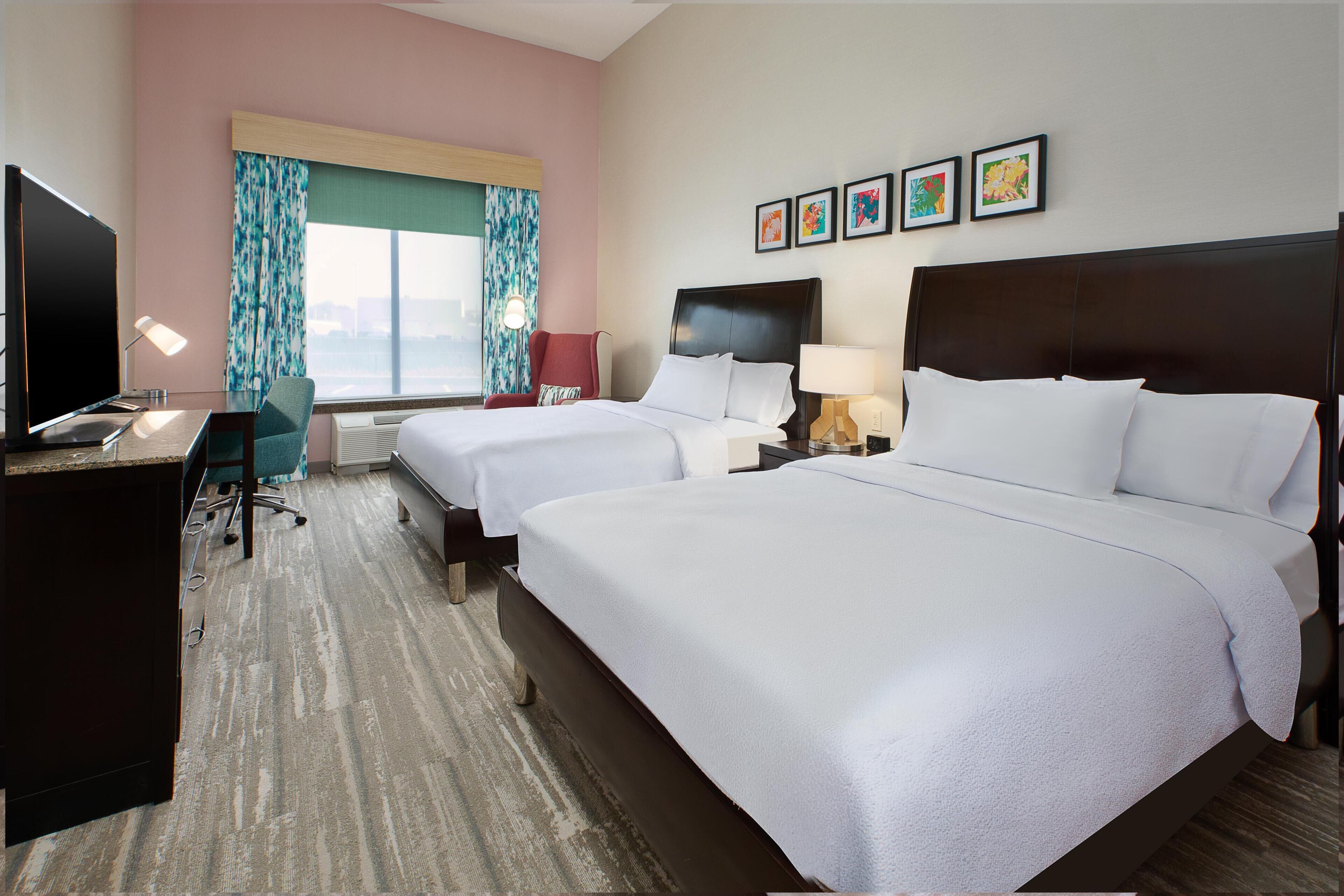 A hotel room with two beds, a desk with a TV, a chair, and a window with curtains.
