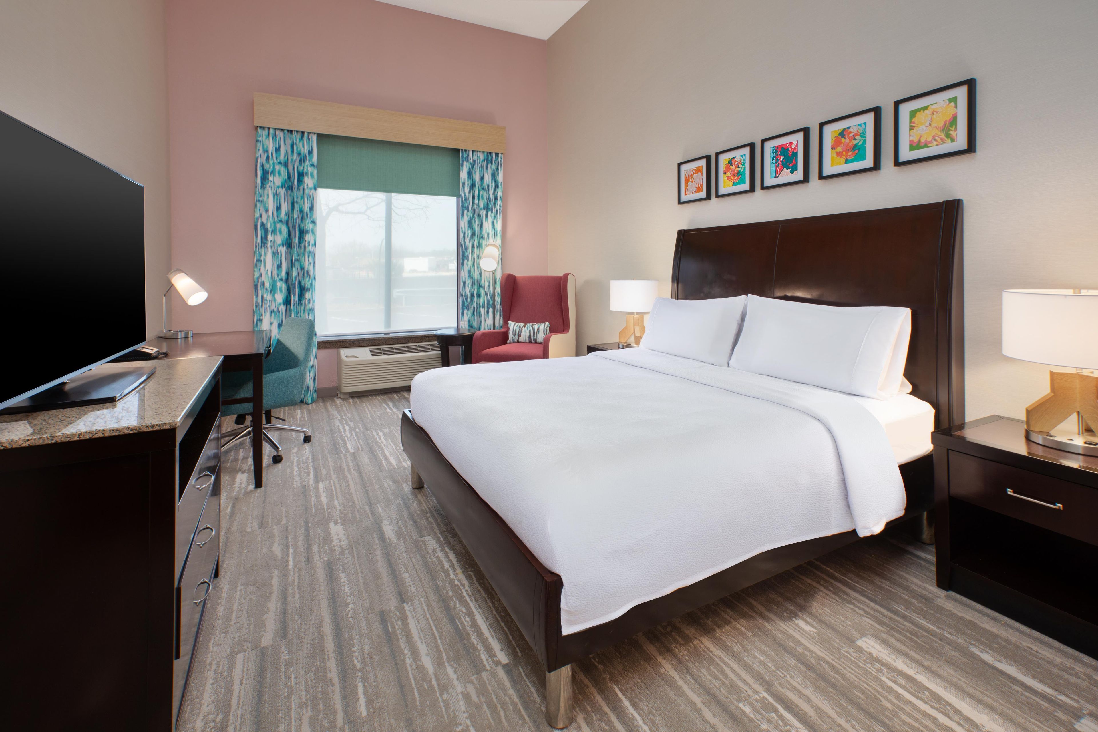 Habitación de hotel con cama, escritorio, silla, televisor y obras de arte en la pared.