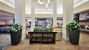 A spacious lobby with a central dining area, large potted plants, and a prominent shop sign. - Hilton Garden Inn Akron (Akron)