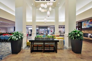 A spacious lobby with a central dining area, large potted plants, and a prominent shop sign. - Hilton Garden Inn Akron (Akron)
