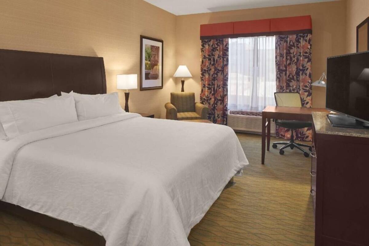 A hotel room with a large bed, a desk with a chair, a television, and a window with curtains.