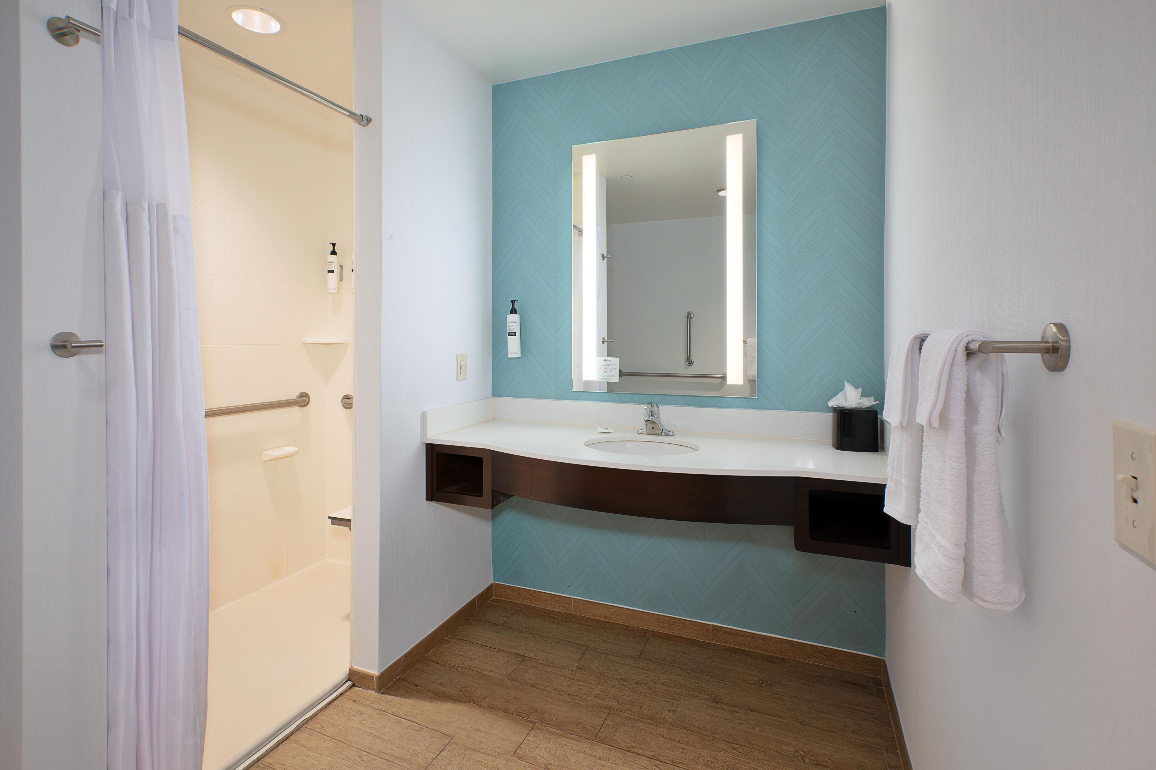 Un baño con ducha, lavabo, espejo y toallero.