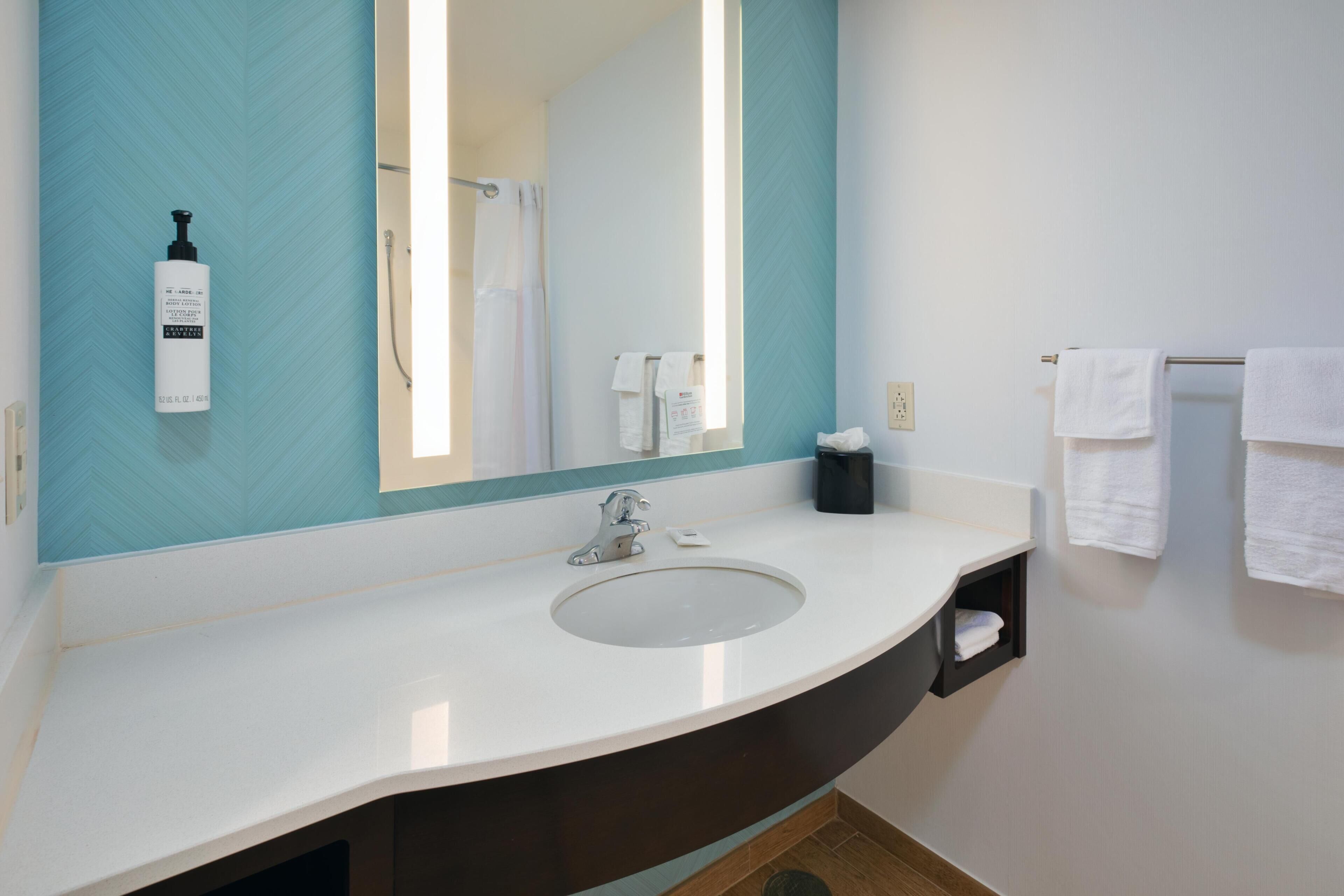 A bathroom with a white sink, a large mirror, a towel rack, and a bottle of shampoo.