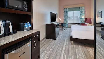 A hotel room with a bed, desk, microwave, coffee maker, and a television.