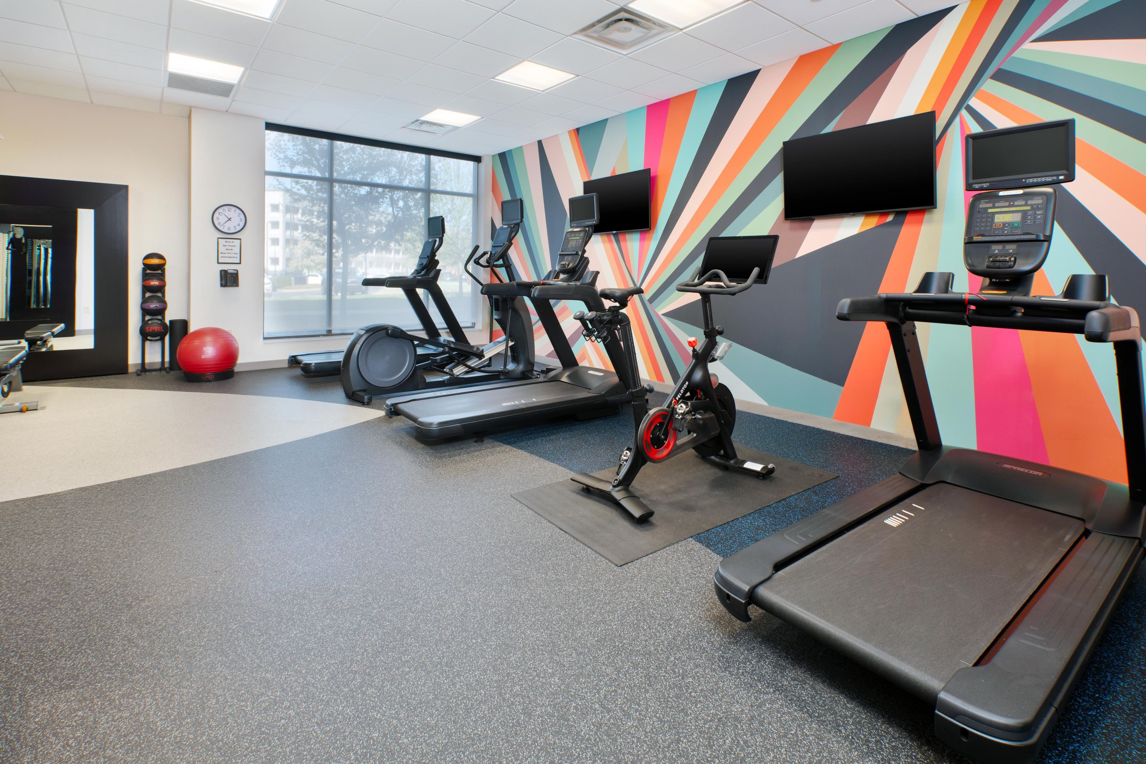 Un gimnasio con cintas de correr, bicicletas estáticas y pelotas de ejercicio.