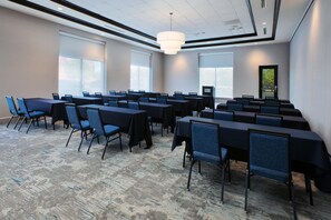 Une salle de conférence avec des rangées de tables et de chaises, de grandes fenêtres et un luminaire au plafond.