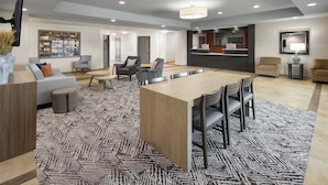 Un amplio vestíbulo de hotel con una mesa central tipo isla, zona de estar y mostrador de recepción.
