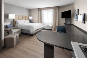 Una habitación de hotel moderna con cama, escritorio, silla, televisor de pantalla plana y aire acondicionado.