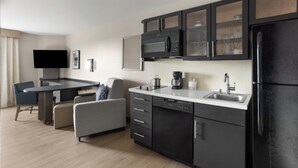 Una cocina moderna con televisión de pantalla plana, microondas, cafetera y refrigerador.