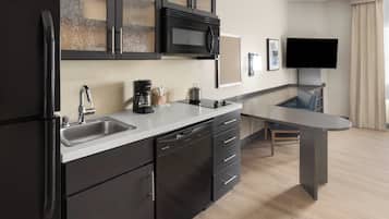 Een moderne keuken met een koelkast, magnetron, spoelbak en vaatwasser. Er is een eethoek met een tafel en stoelen. Een flatscreen televisie is aan de muur bevestigd.