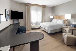 Habitación de hotel moderna con cama, mesitas de noche, escritorio, televisor de pantalla plana y un amplio ventanal con cortinas.
