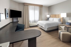 Quarto de hotel moderno com cama, mesas de cabeceira, escrivaninha, televisão de tela plana e uma grande janela com cortinas.