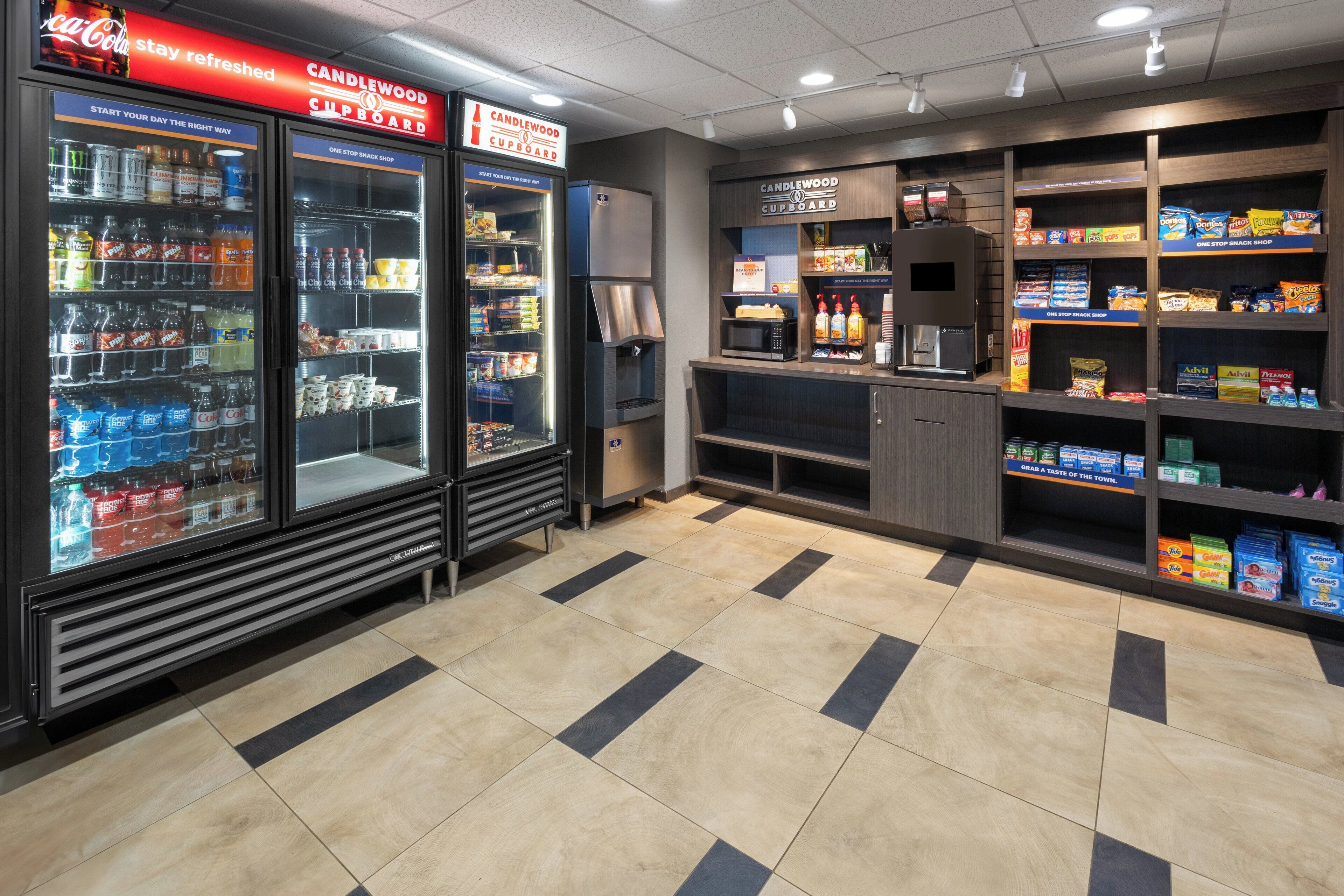 Un bar de aperitivos limpio y bien iluminado, con una variedad de bocadillos y bebidas, incluyendo un refrigerador de Coca-Cola y un microondas.