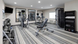 Un gimnasio con máquinas de cardio, pesas libres y un espejo grande.