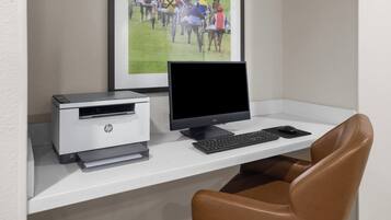 A workspace with a printer, monitor, keyboard, and chair.