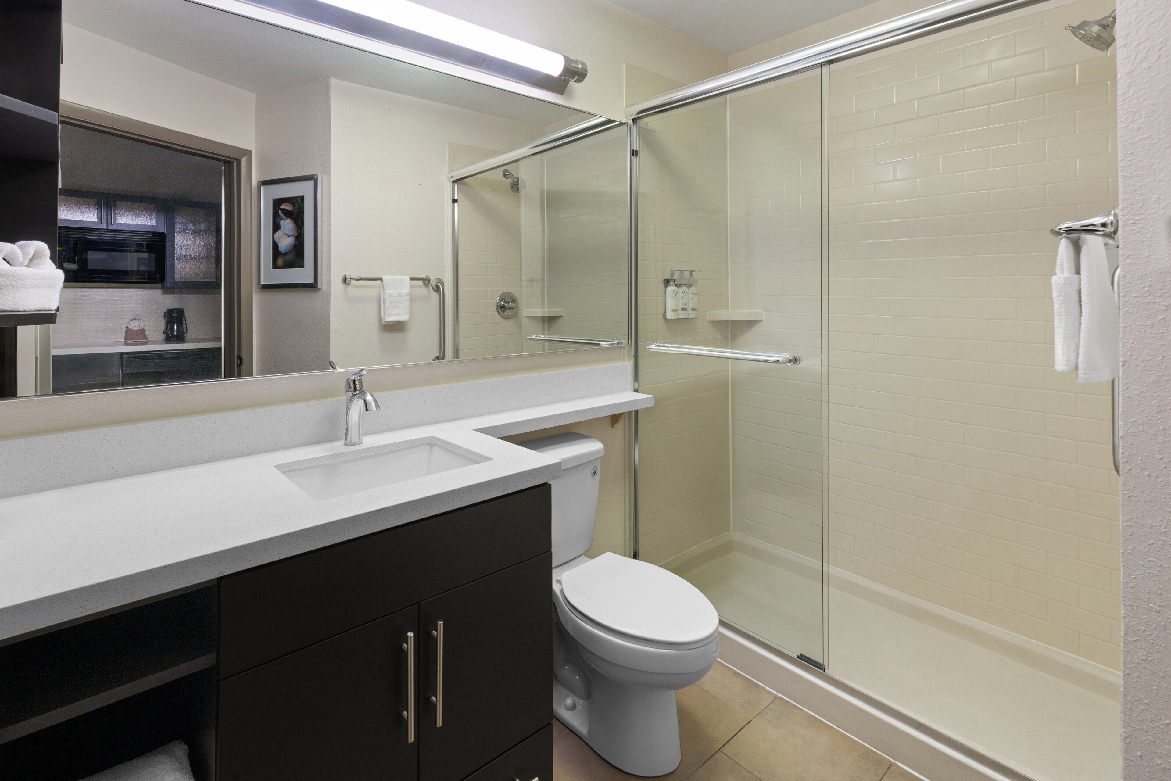 Un baño moderno con cabina de ducha de vidrio, un lavabo blanco y un mueble de tocador de tonos oscuros.