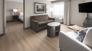 Una habitación de hotel moderna con sofá, una mesa de centro redonda, televisión y una cama con mesita de noche.