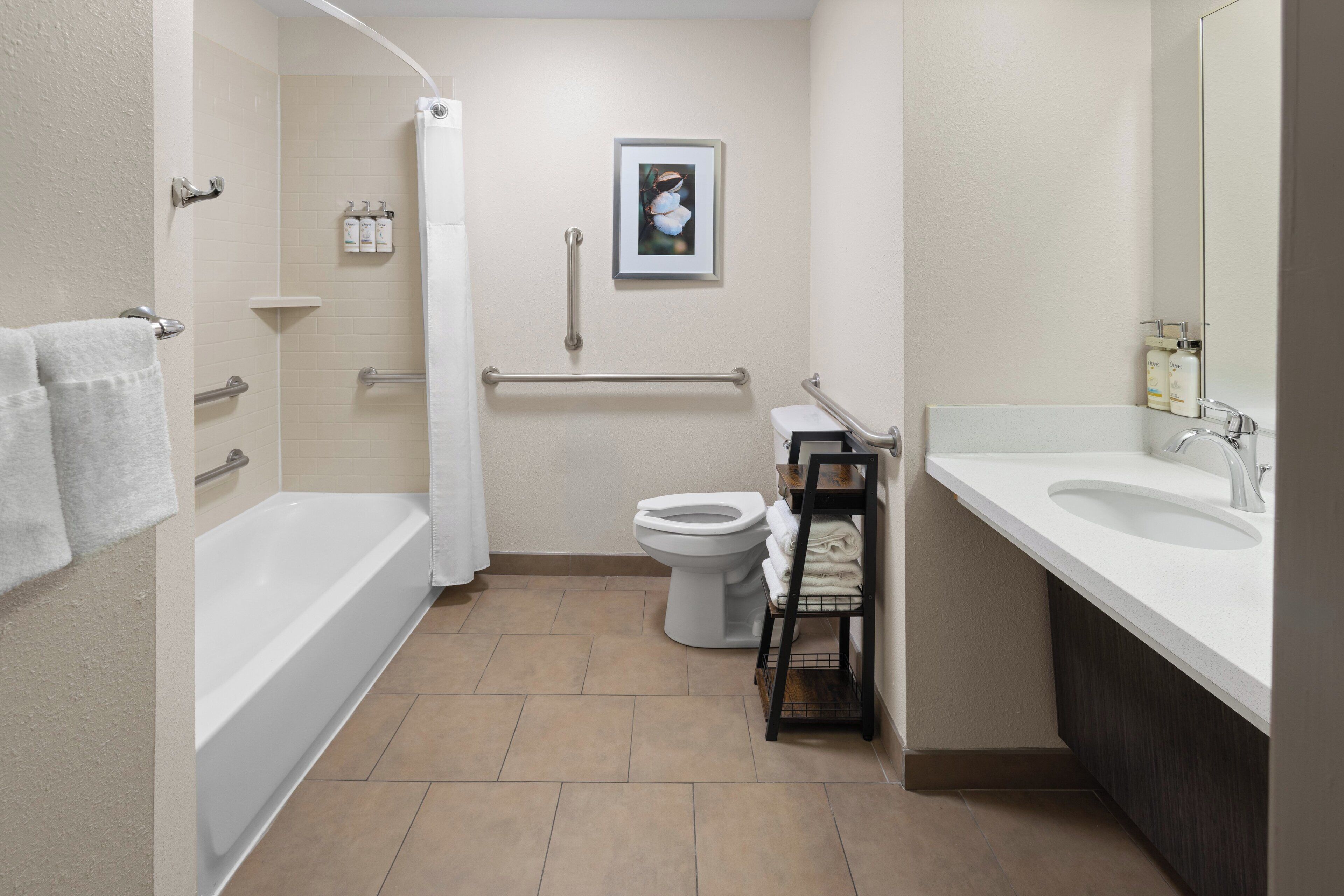 Un baño moderno con bañera, inodoro y lavamanos. Incluye barras de apoyo y cortina de ducha.